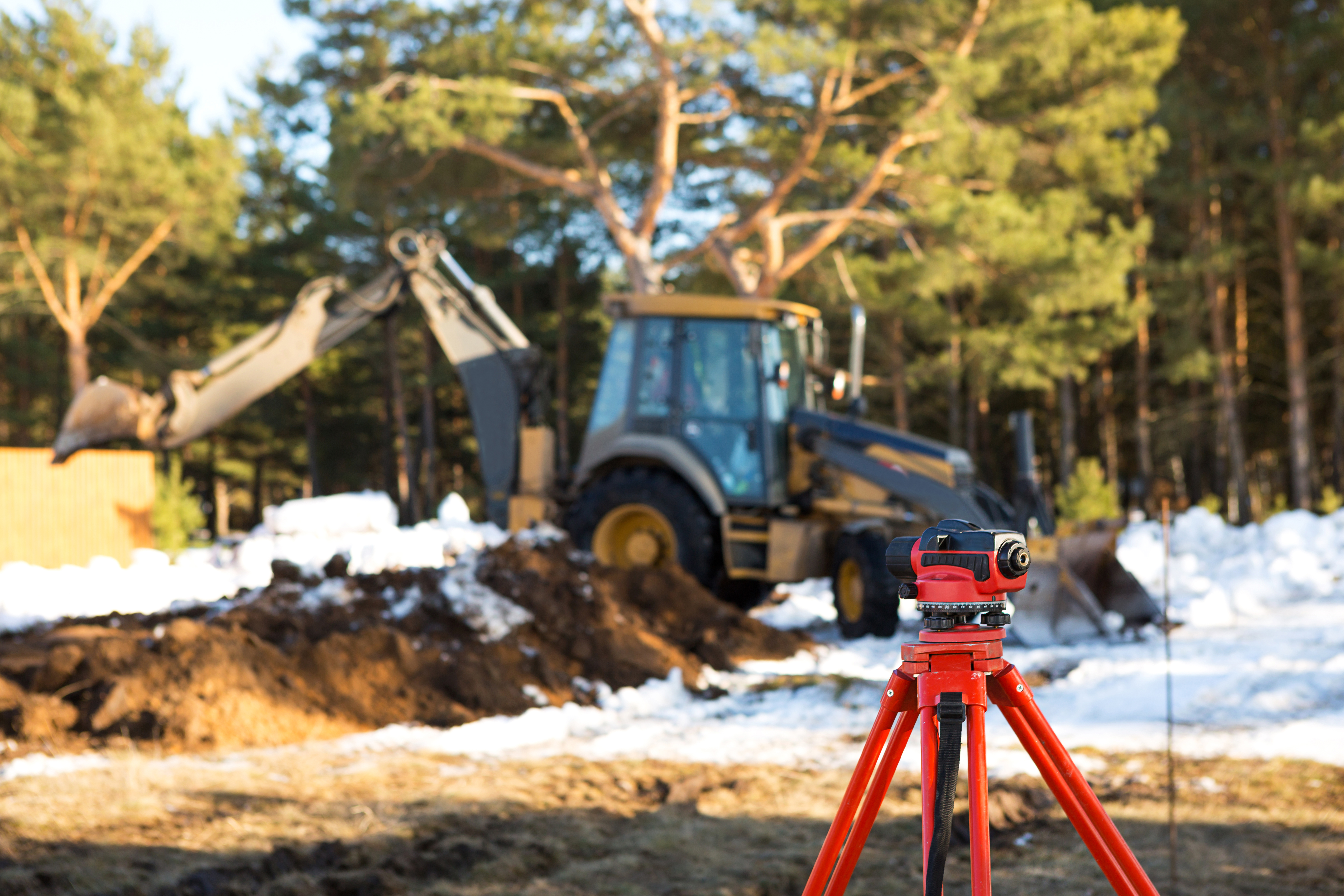 A geodesic level stands in front of a bulldozer for excavating a pit at a construction site